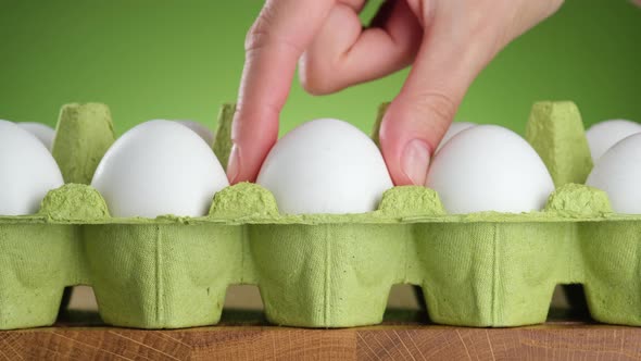 Hand takes white egg from green egg packing
