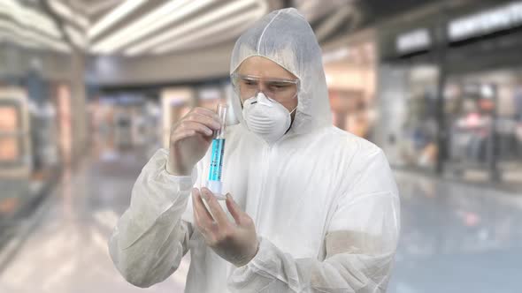 Man Wearing Antiviral Protective Suit Holding Test Tube with Blue Medicine