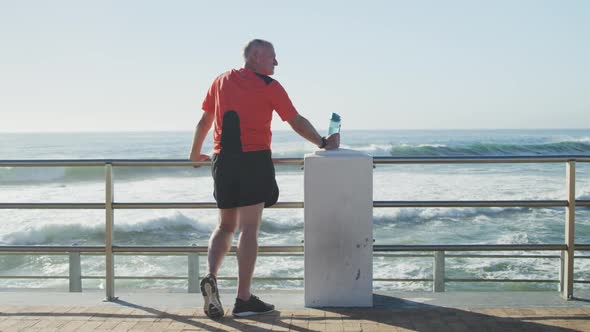 Senior man holding water bottle standing on the promenade