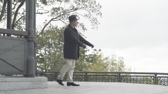 Wide Shot of Nervous Elegant Caucasian Man Walking and Thinking Outdoors on Cloudy Day. Camera