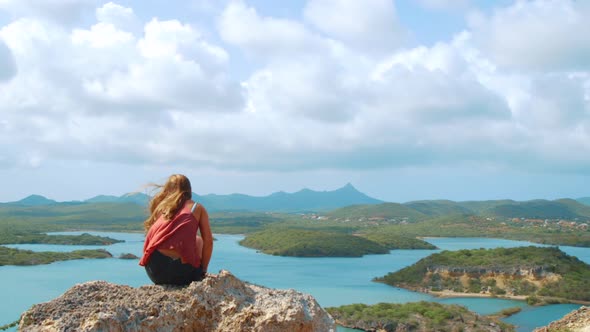 Young woman sitting down on mountain above Santa Martha Bay, Curacao, SLOWMO