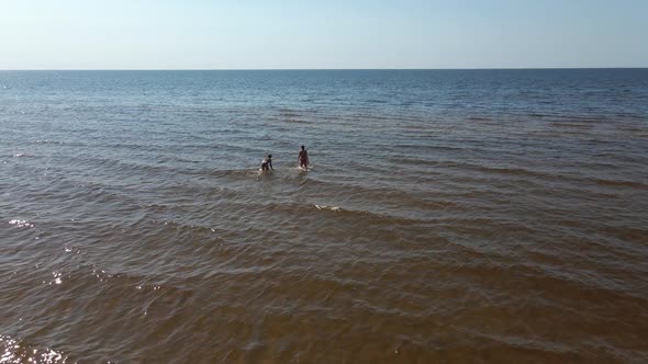 Backside Aerial View: Two Women in Swimsuits Walking Away in Sea