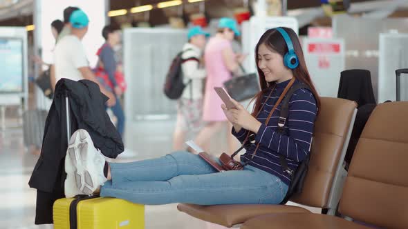 Young female traveler listening music from headphone at airport