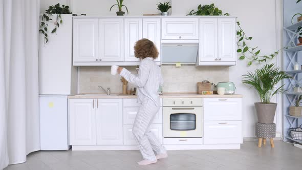 Young Woman Dancing And Using Cellphone In Kitchen.