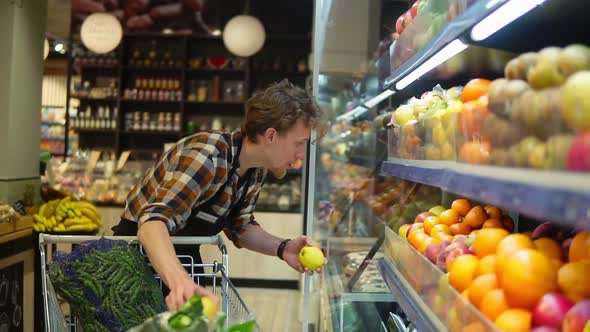At the Supermarket Handsome Stock Clerk Wearing Black Apron Arranging Organic Fruits and Vegetables