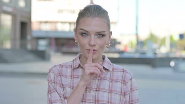 Outdoor Young Woman with Finger on Lips Please Be Quiet