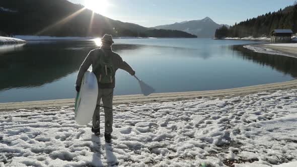 Man carrying SUP through snow to a lake