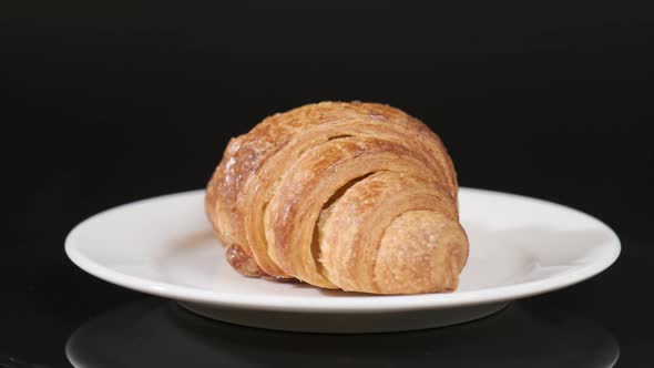Croissant on white plate rotating in front of camera on black background
