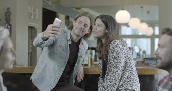 Man holding mobile phone and smiling while sitting with woman in pub