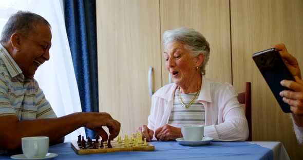 Senior woman using digital tablet while her friends playing chess 4k