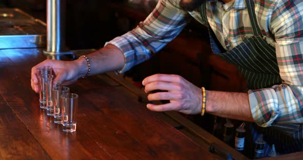 Barman arranging shot glasses at bar counter