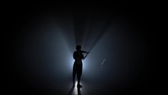 Woman Plays the Violin and Looks at the Music Stand in the Dark . Silhouette. Black Smoke Background