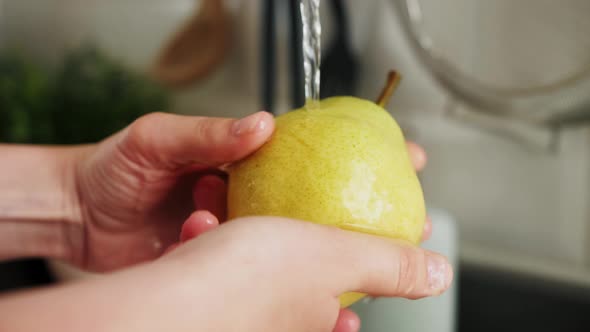 Hands washing the fruit under running clean water.