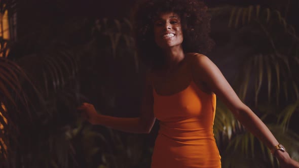 Smiling Woman With Afro Hair Dancing To Camera In Orange Dress