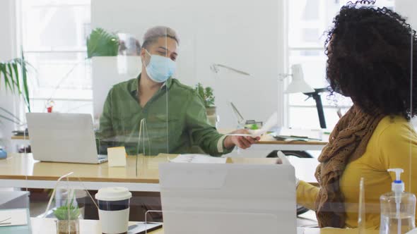 Man wearing face mask passing a document to his colleague at office