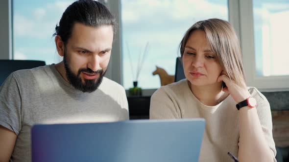 Two Coworkers are Discussing a Project While Sitting in Front of Their Laptops