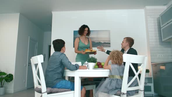 Young and beautiful husband and wife and children are sitting at the family table and smiling