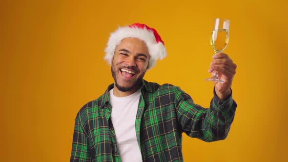 African American Male in Santa Hat Raising a Glass of Champagne Against Yellow Background