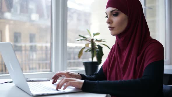 Young Attractive Supposedly Muslim Girl Typing Something on Her Laptop alt