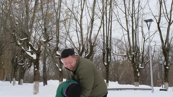 A Young Father Plays with His Little Son in a Winter Park