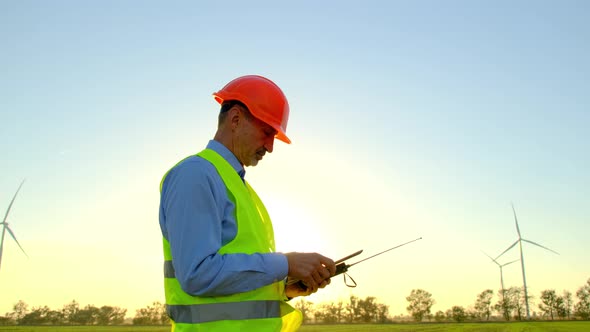 Windmills Examined By Engineer with Tablet at Rural Station