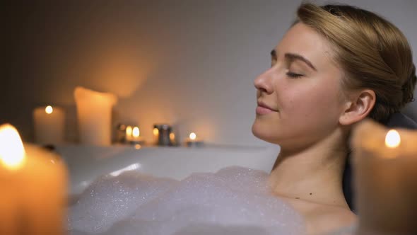 Young Female Relaxing in Warm Bath With Foam Bubbles and Candles, Evening