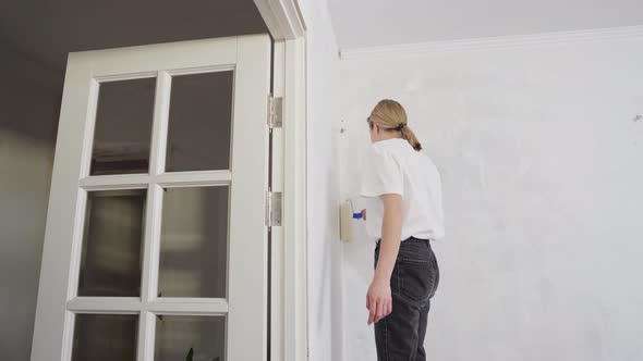 a Young Woman Paints a Wall in an Apartment with a Roller