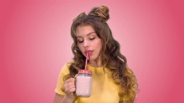 Beautiful Young Girl with a Styling is Drinking Smoothies and Smiling While Looking Into the Camera