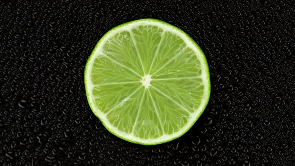 Lime on black background with water drops, rotate. 4K UHD video