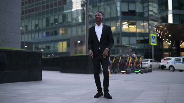 Young black guy in a suit is dancing on the background of the business center