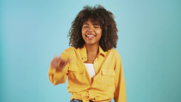 Young Ethnic Black Lady Laughing and Showing Loser Hand Gesture While Posing Against Blue Studio