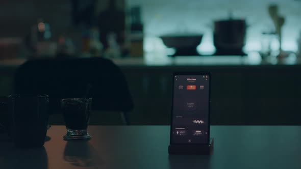 Smart Home Application on Phone Placed on Kitchen Desk in Empty House