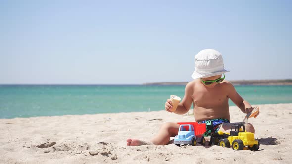 on a Sunny Hot Summer Day, a Boy Plays with Sand and Toys, Cars on the Beach