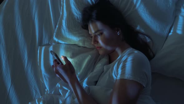 Indifferent Apathetic Young Woman Lying on Bed and Using Smartphone