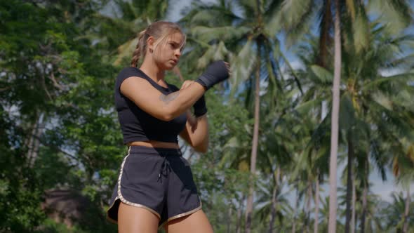 Closeup of Young Strong Female in Black Sportswear Practicing Boxing with Hands in Fingerless Gloves
