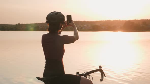 Cyclist looking at sunset and taking photos on smartphone