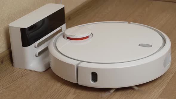 White Robotic Vacuum Cleaner Finishes Cleaning And Drives to Its Charging Station