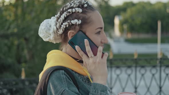 Young Woman Walking at Street and Talking on Phone. Woman with Pigtails