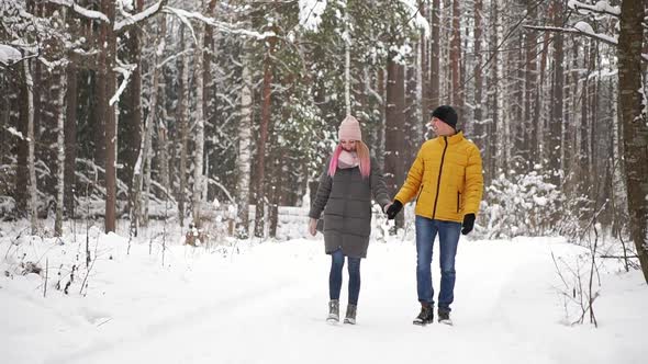 A Man in a Yellow Jacket and a Girl in a Hat and Scarf Walk Through the Winter Forest During a