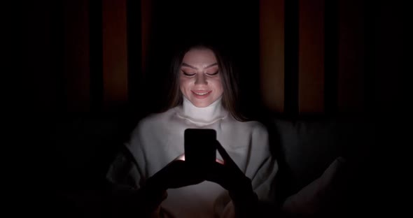 Young Female Lying on the Bed and Uses Smartphone Types Text Night Time Online Communication