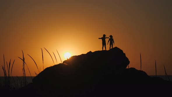 Children Silhouettes Against the Sunset. Boys in Hats with Brims Stand on a Rock. The Stone Lies on