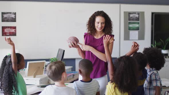 Video of happy caucasian female teacher and diverse school children studying biology in classroom