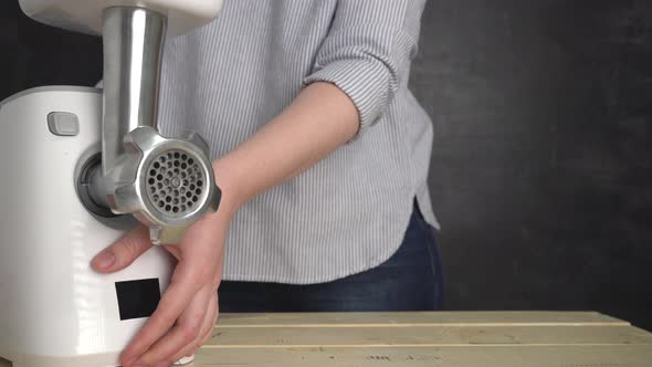 The girl puts an electric meat grinder on the table and shows a nozzle for cooking sausages