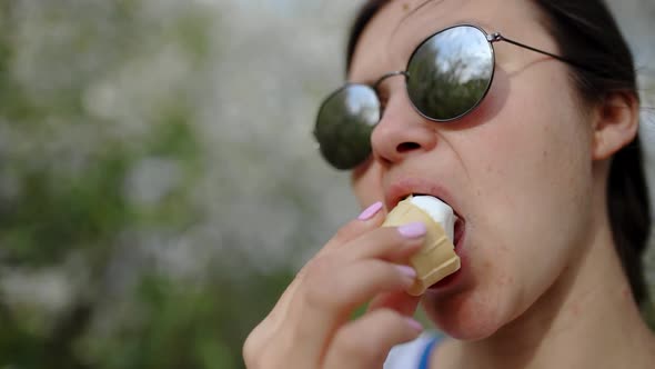 A Beautiful Girl in Sunglasses Eats Ice Cream in a Blooming Garden