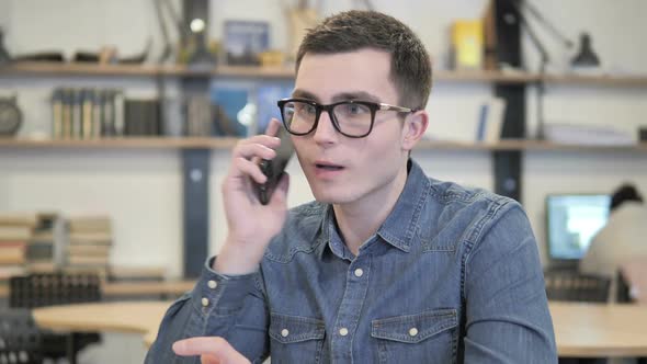 Creative Young Man in Glasses Talking on Phone and Discussing Work