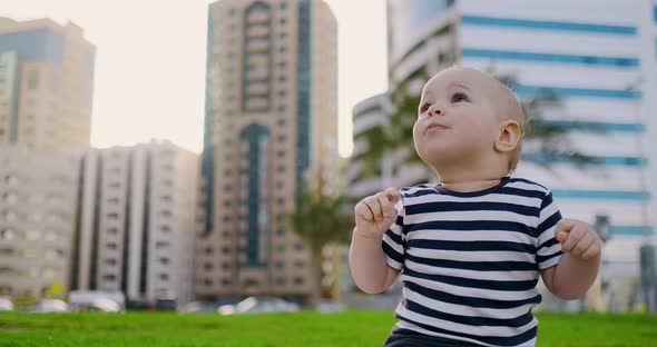 The Child Sits on the Grass in the Summer and Laughing Clapping