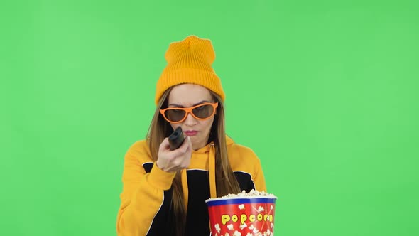 Portrait of Girl in Yellow Hat in 3D Glasses Is Watching TV and Eating Popcorn with TV Remote in Her