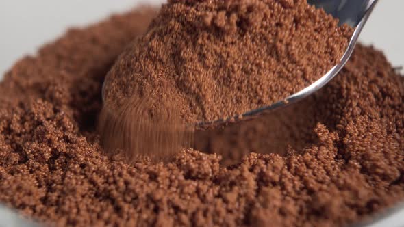 A hand with a shiny dessert spoon scoops instant chicory powder 