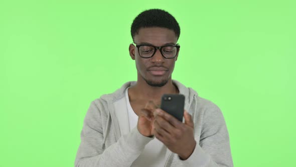 African Man Browsing Smartphone on Green Background