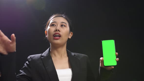Speaker Woman In Business Suit Holding And Pointing Green Screen Smartphone In The Black Studio